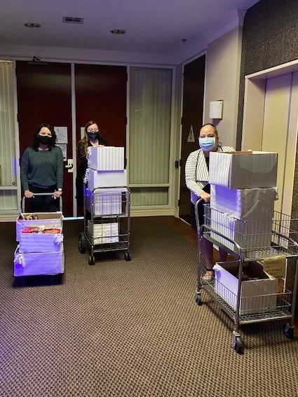 Three women hold on to metal carts piled high with boxes filled with gifts.