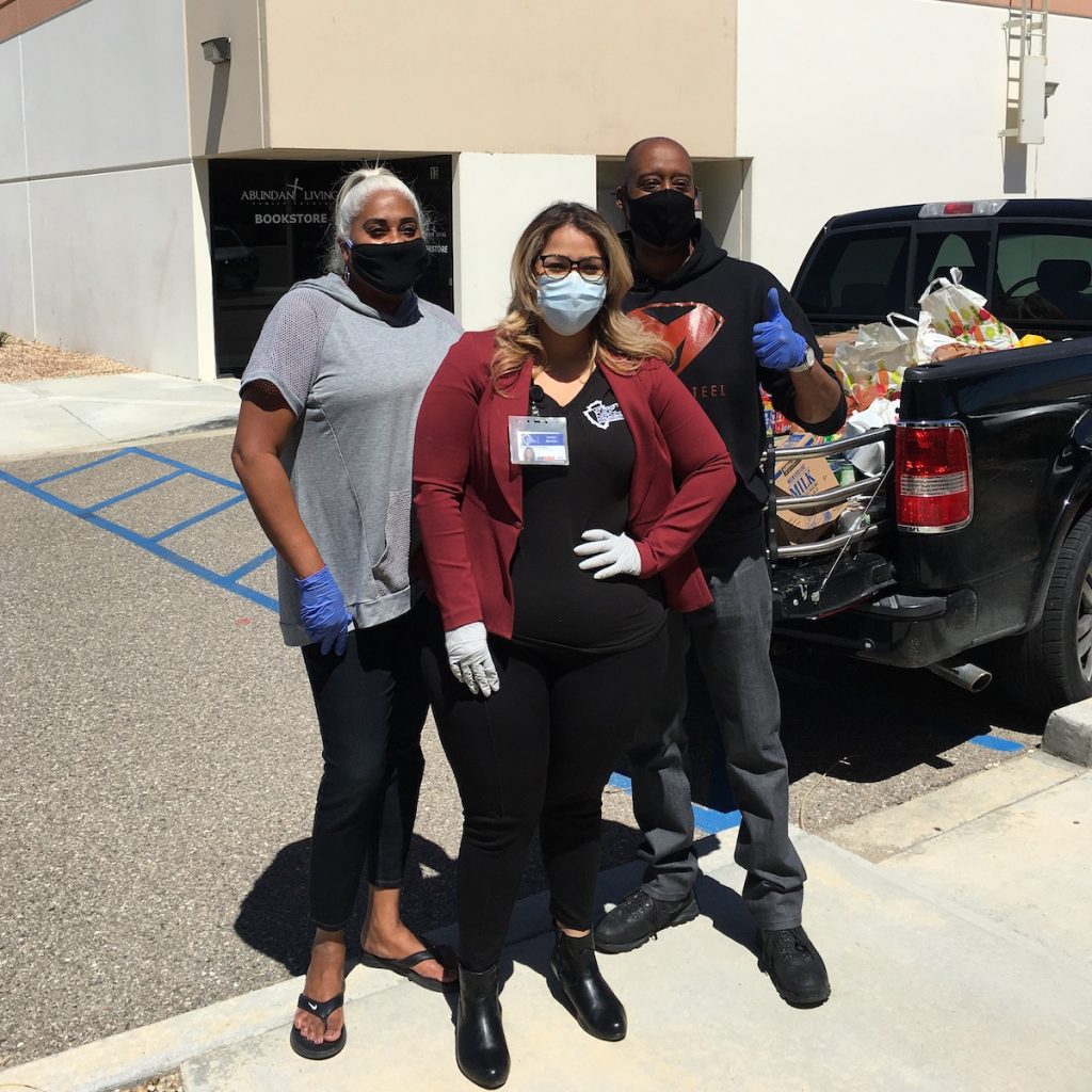 Three people wearing face masks pose next to a pickup truck filled with boxes of supplies.