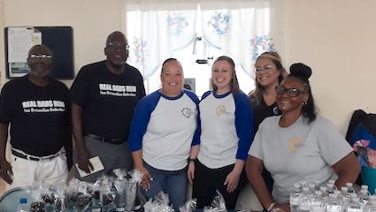 A group of six representatives from San Bernardino Fatherhood and the San Bernardino County Public Defender's Office stand smiling behind a table lined with giveaways.