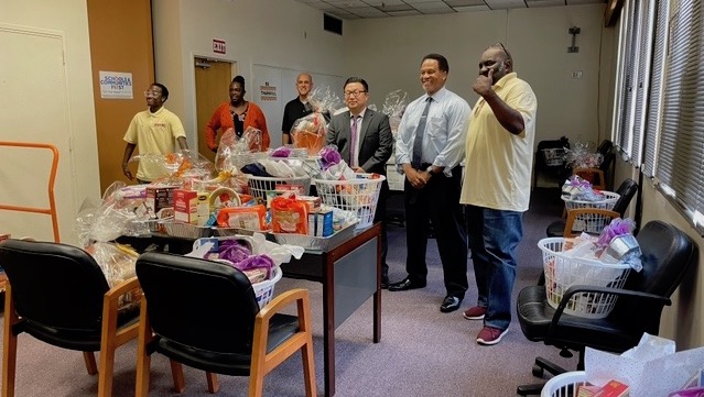 A group of six people stand around a table piled with Thanksgiving baskets.