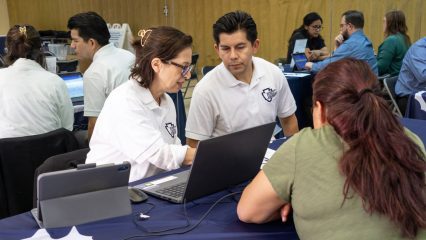 Public Defender staff assist a community member at a Mobile Defense event with laptops and informational materials.