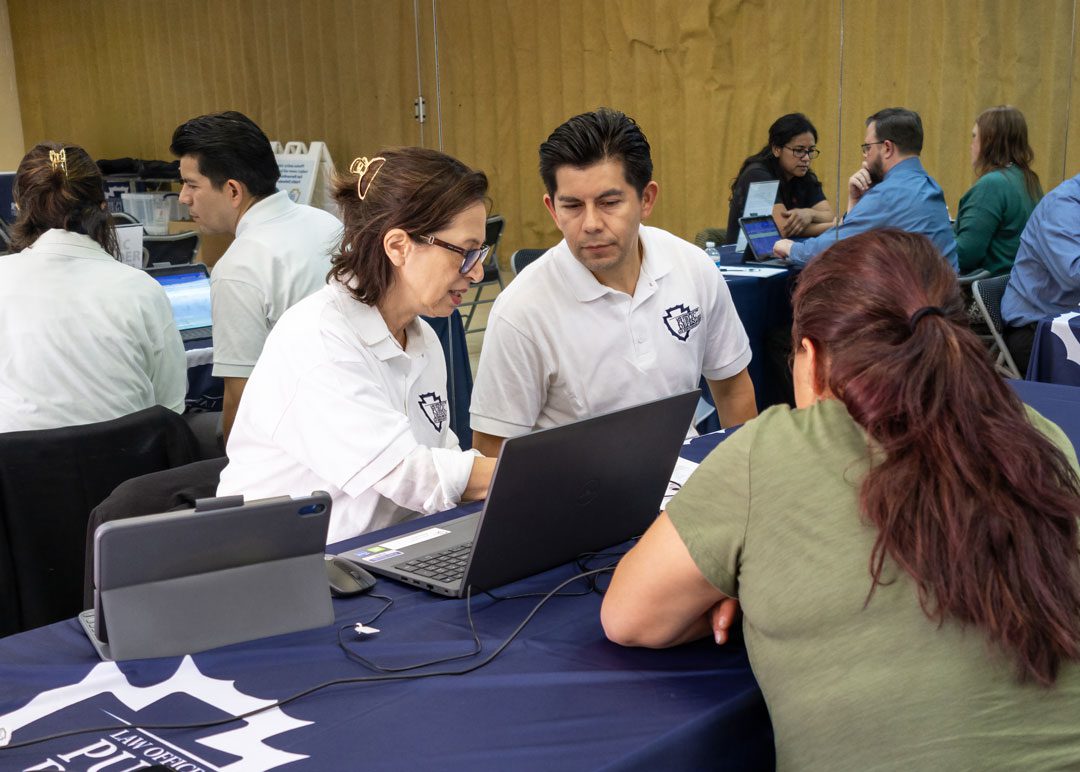 Public Defender staff assist a community member at a Mobile Defense event with laptops and informational materials.